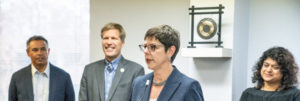 Tracy Hartzler, CNM President, standing at a podium while Mayor Keller and two others look on.