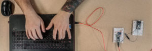 Arial view of a man typing on a laptop that is connected to circuits.