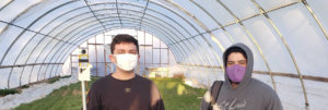 two students in greenhouse holding soil monitoring equipment