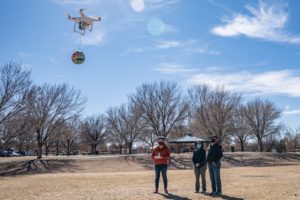 three people stand in field flying drone