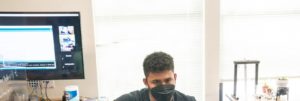 Student in IoT bootcamp hold right hand out with smartglove covered in wires. Looking at laptop.