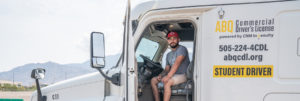 CDL student sits behind the wheel with door open, posing for picture